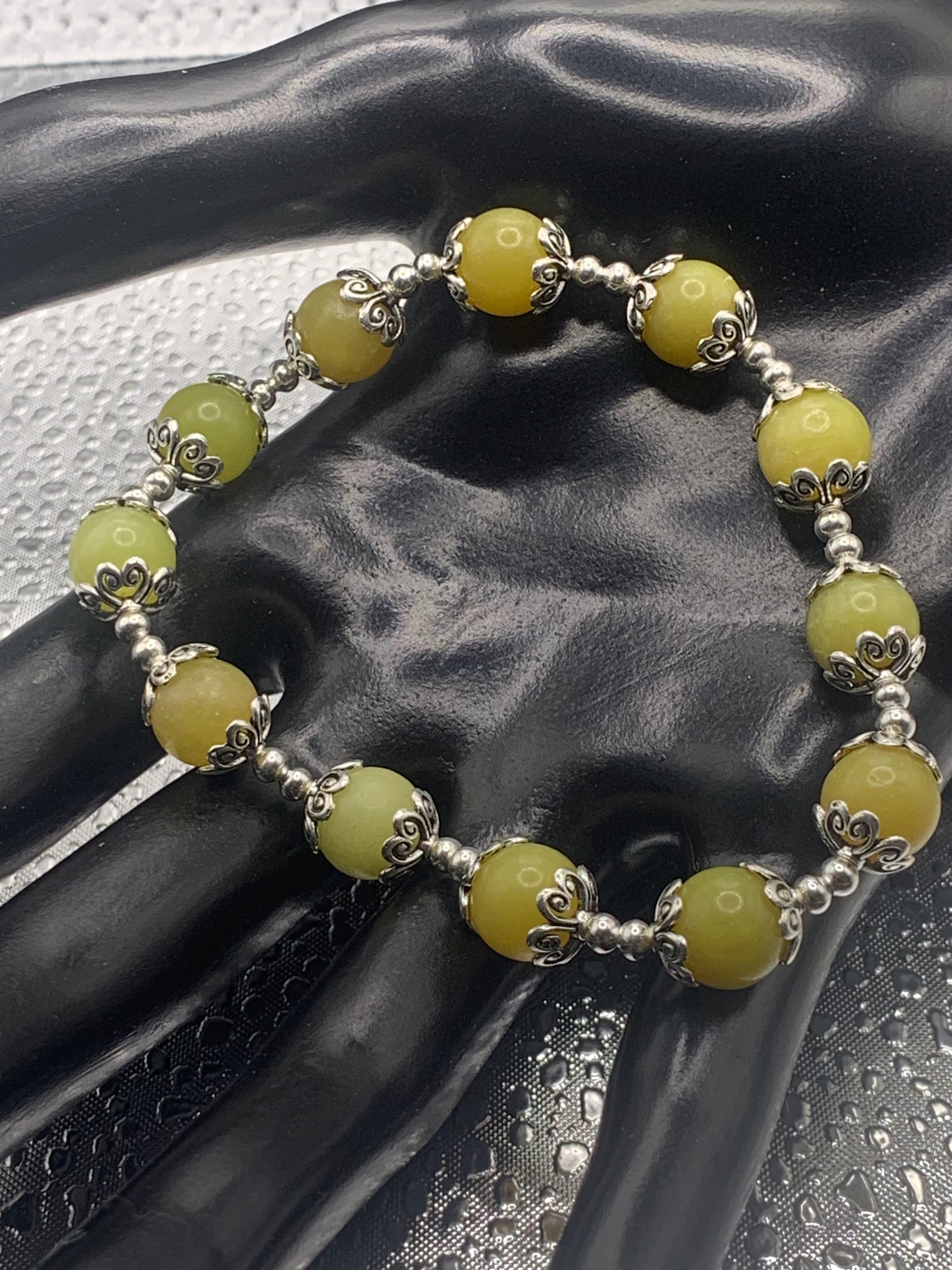 This bracelet contains yellow jade beads that are surrounded by bead caps and spacer beads